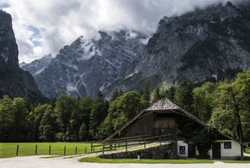 Una casa antigua alrededor de un bosque de pinos verdes bajo una montaña en los Alpes. Konigssee, Alemania