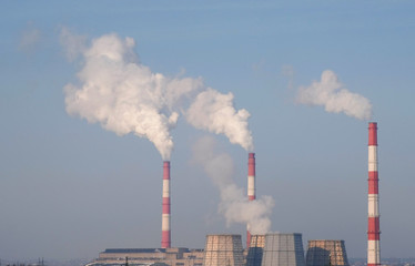 Thermal power station with three red and white pipes with smoke in sky background.