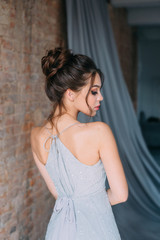Young girl in a gray, evening dress posing on the camera. Bright evening make-up with long...