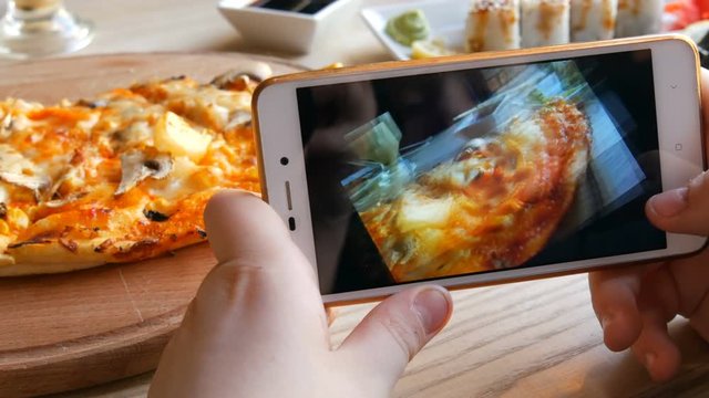 Teenager boy takes a photo of food on a smartphone. Japanese sushi rolls and Italian pizza on the restaurant table