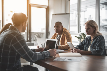 Four calm people sitting at meeting and using gadgets. They having undistracted expressions
