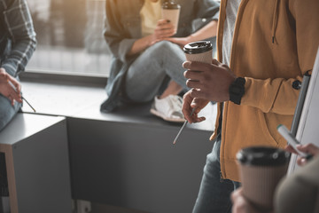 Men and women resting with paper cups in hands while taking break at work. Close up