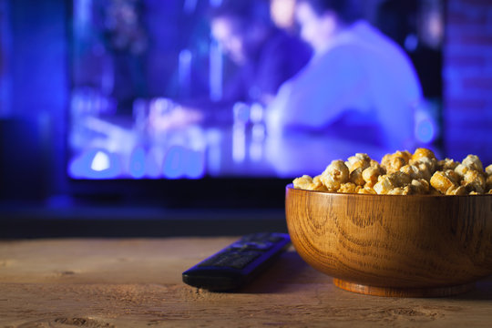 A Wooden Bowl Of Popcorn And Remote Control In The Background The TV Works. Evening Cozy Watching A Movie Or TV Series At Home