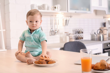 Cute little boy with cookies sitting on table in kitchen