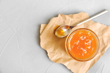 Jar and spoon with sweet jam on textured background