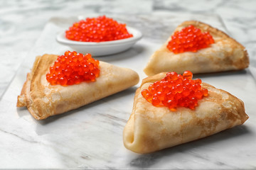 Thin pancakes with delicious red caviar on table