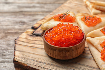 Bowl with delicious red caviar and thin pancakes on wooden board