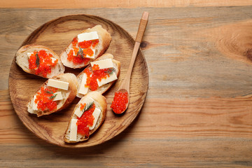 Delicious sandwiches and spoon with red caviar on wooden plate, top view