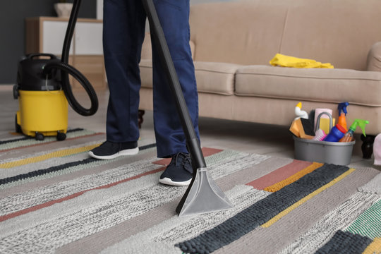 Mature man hoovering carpet with vacuum cleaner in living room