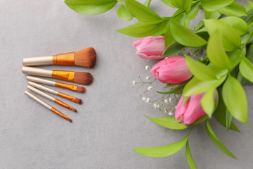 Fototapeta na wymiar Makeup brushes and flowers on grey background