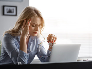 Exhausted young woman feeling pain in head after working on laptop. She is touching temple with frustration. Overwork concept