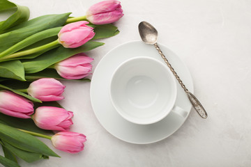 Fototapeta na wymiar Empty white cup of coffee and a bunch of pink tulips on the pastel white table background, top view, flat lay