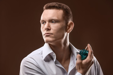 Handsome man in shirt using perfume on dark background