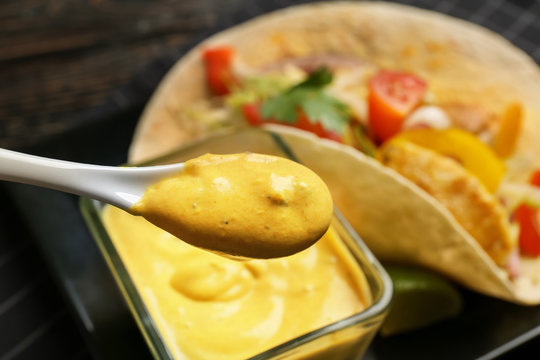 Spoon with tasty creamy sauce for fish taco on blurred background