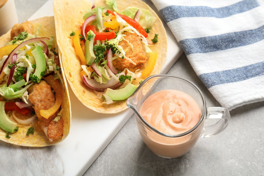 Tasty creamy sauce in jug and fish tacos on kitchen table