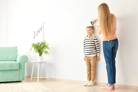 Young Woman Measuring Height Of Little Boy At Home