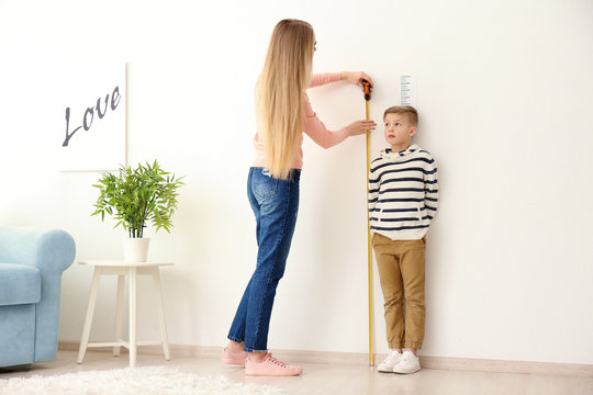 Young Woman Measuring Height Of Little Boy At Home