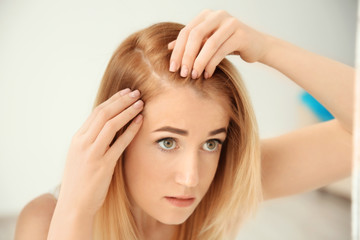 Young woman with hair loss problem on light background