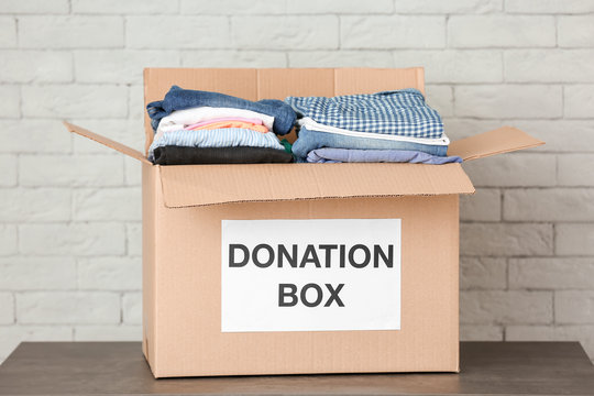 Donation box with clothes on table against brick wall