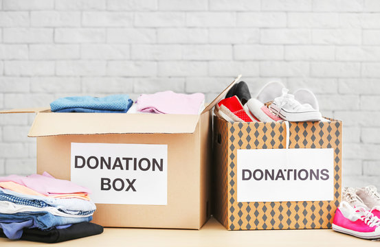 Donation boxes with clothes and shoes on table against brick wall
