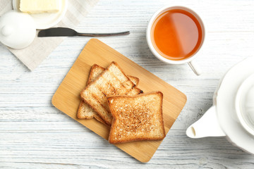Fototapeta na wymiar Board with toasted bread and cup of tea on wooden background, top view
