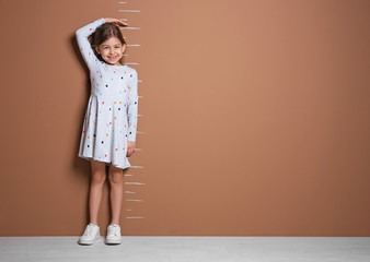 Little girl measuring her height near color wall