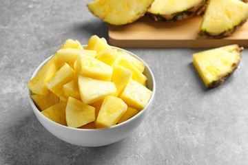 Bowl with fresh pineapple slices on grey background