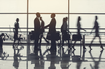 Full length side view glad businessmen shaking hands while meeting at job. Different female and male colleagues going there. Salutation at labor concept