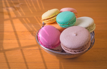 French macarons  in a metal cup on a wooden background. Sunlighted by sunlight