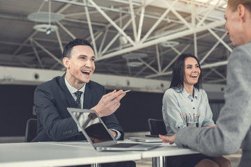 Portrait of laughing male and cheerful woman speaking with affiliates while locating at desk indoor. Glad workers during job concept