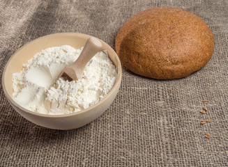 Wheat ears, wooden bowl with flour on a fabric background
