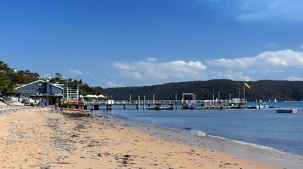 Fototapeta na wymiar Sydney, Australia - Sept 10, 2017. The Boathouse Palm Beach cafe restaurant at the west side of Palm Beach, Pittwater. People, family with kids relaxing, sunbathing on the beach.