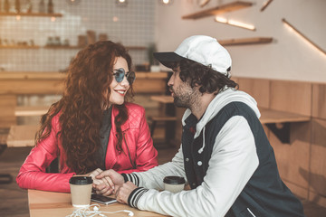Happy loving couple is holding hands with gentleness while dating in cafeteria. They are looking at each other with love and smiling