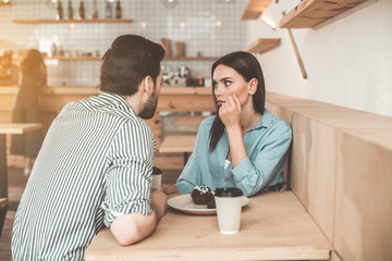 Shocked news. Surprised young woman is talking with man in cafe. She is looking at him with...