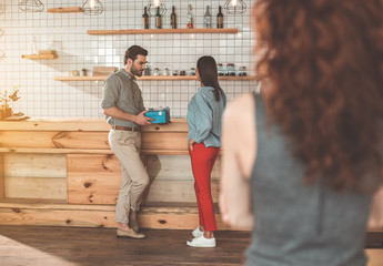 Seductive man giving present to young girl in coffee shop. Jealous woman is looking at them from the side