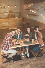 Top view of carefree guys and girls chatting in coffee shop. They are looking at camera and laughing