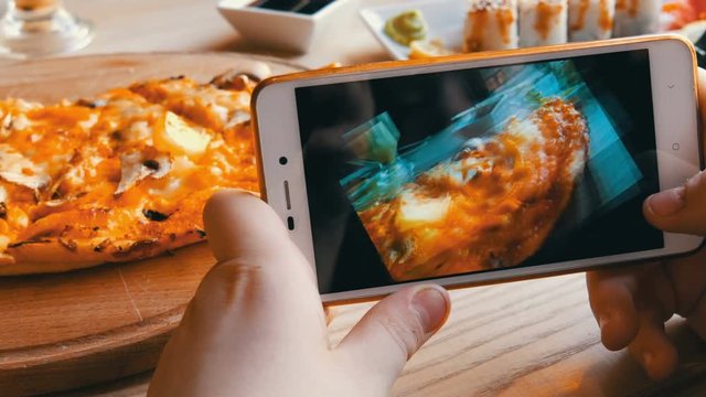 Teenager boy takes a photo of food on a smartphone. Italian pizza on the restaurant table