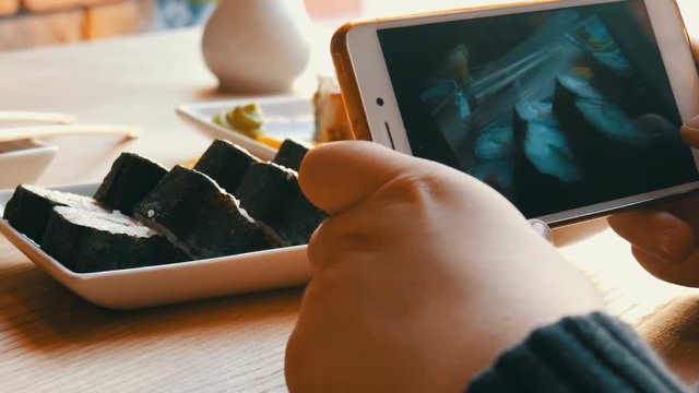 Teenager boy takes a photo of food on a smartphone. Japanese sushi rolls on the restaurant table