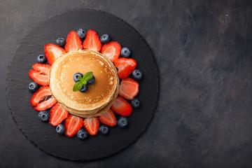 Delicious pancakes close up, with fresh blueberries, strawberries on a black stone background. Top view with copy space