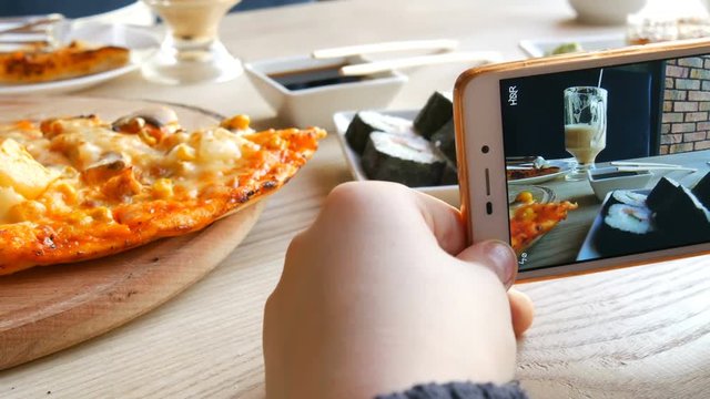 Teenager boy takes a photo of food on a smartphone. Japanese sushi rolls and Italian pizza on the restaurant table