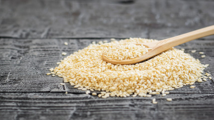 Sesame seeds in a white spoon of light wood on a dark table.