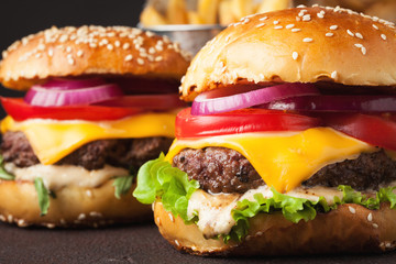 Close-up of delicious fresh home made burger with lettuce, cheese, onion and tomato on a dark background. fast food and junk food concept
