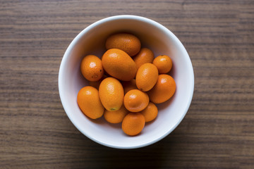 Top View of Orange Organic Kumquats with White Bowl on Wood Table