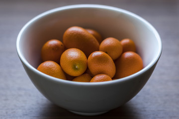White Bowl of Orange Organic Kumquats on Wood Table