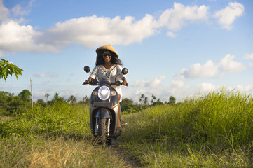 Plakat young beautiful tourist or nomad traveler black afro American woman riding motorbike in tropical field wearing traditional Asian hat smiling happy