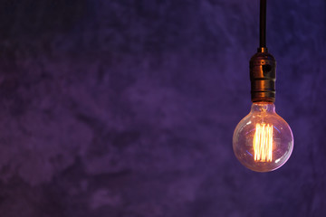 Front side view of vintage tungsten filament lamp hanging from the ceiling of purple and blue...
