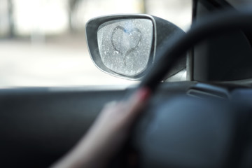 The symbolic image of the heart on a dusty car rearview mirror