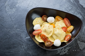 Black bowl with italian ravioli pasta on a grey concrete background, elevated view, horizontal shot