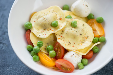 Closeup of ravioli with addition of green peas, cherry tomatoes and mozzarella balls, selective focus