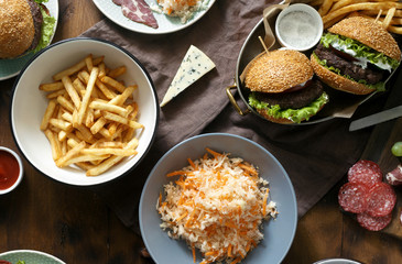 Delicious outdoor table with burger, french fries, salad and snacks on wooden table, top view. Outdoors food Concept
